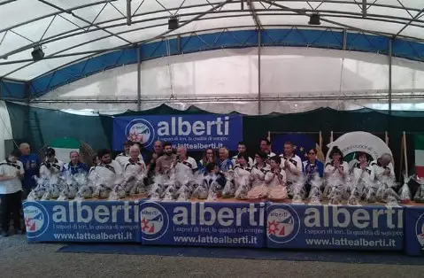 Foto di gruppo degli Arcieri Imperiesi sotto una struttura di tiro, davanti ai bersagli e agli striscioni