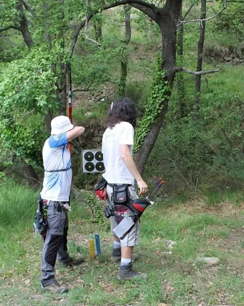 Due arcieri sul percorso nel bosco: uno tende l'arco verso il bersaglio